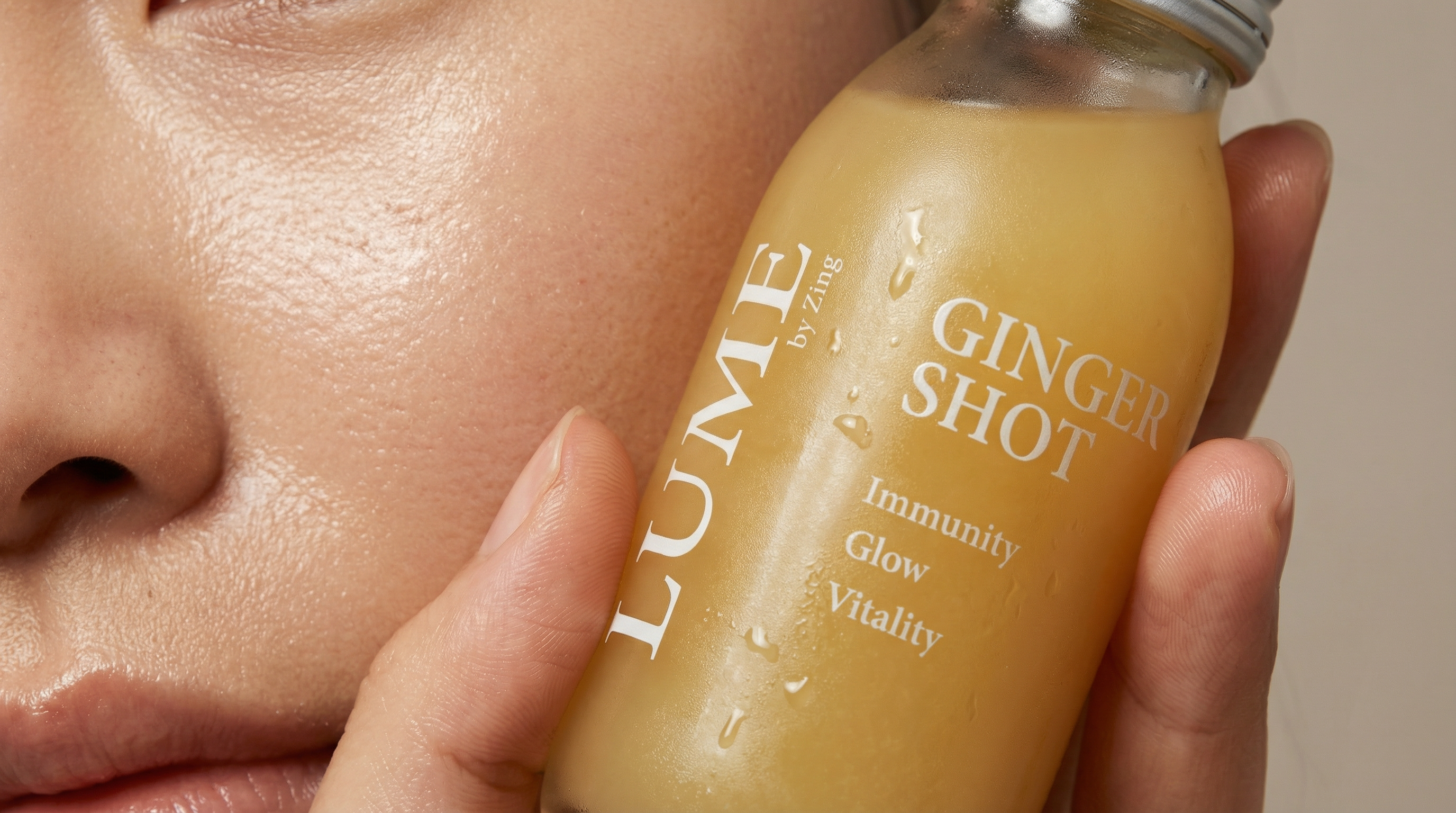 Woman holding a chilled LUME ginger shot bottle against her face — natural glow and skin wellness